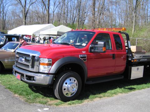 1991 Ford LTD Crown Victoria - A red Ford F-550 tow truck is parked next to another vehicle under tents.