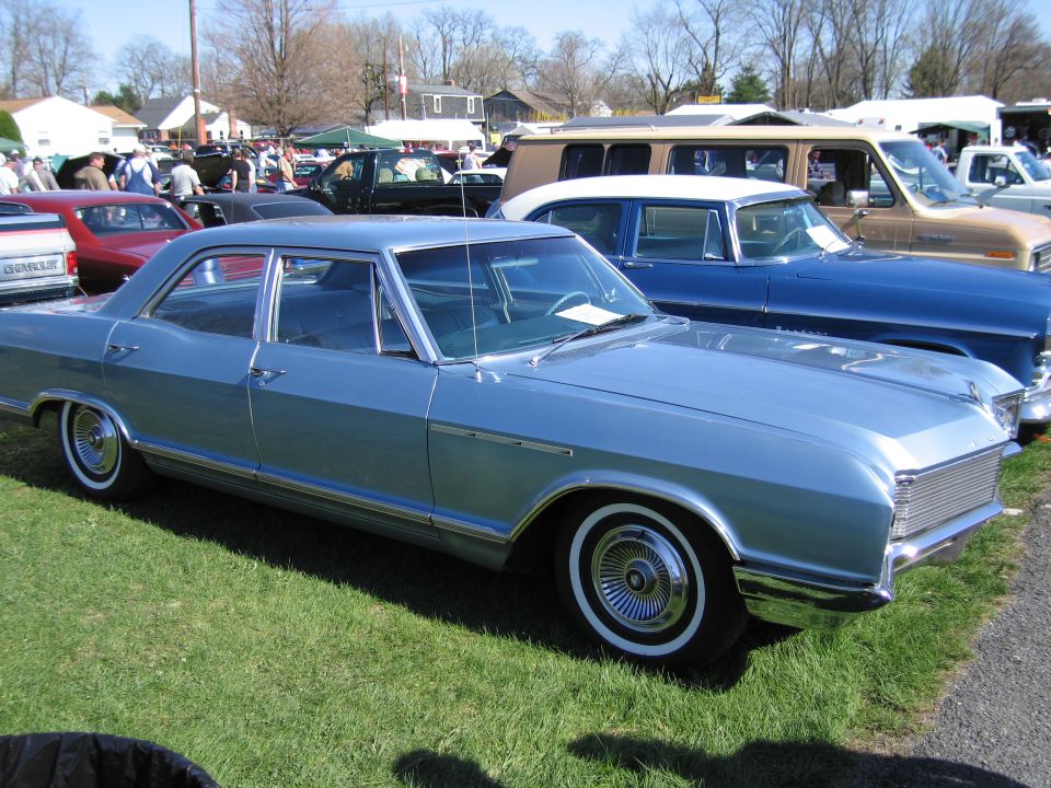 Light blue sedan parked on grass, side view. Chrome trim, whitewall tires, and a distinctive grille are visible