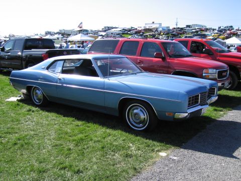 1991 Ford LTD Crown Victoria - A light blue coupe from the early 1970s is parked at an outdoor event with other vehicles and tents in the background.