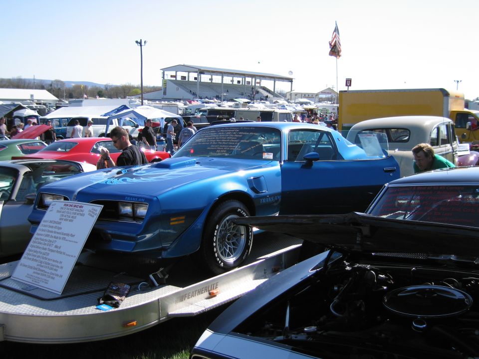 Blue 1979 Pontiac Firebird Trans Am with hood scoop and open door, parked on a trailer at a car show