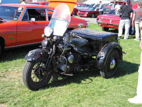 1991 Ford LTD Crown Victoria - A black three-wheeled motorcycle with a sidecar is parked on a grassy field, with other cars in the background.