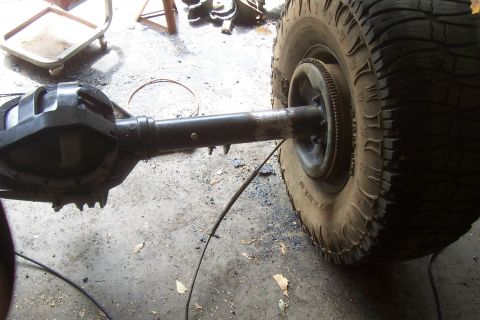 1994 Ford F-150 - solid front drive axle with differential and one mud-terrain tire mounted sits on a garage floor during a swap.