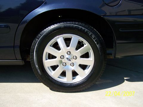 2003 Ford Crown Victoria - Close-up of a dark blue car's rear wheel and fender, a silver 5-spoke Ford alloy rim.