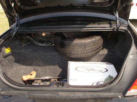 2001 Ford Crown Victoria - The trunk of a car contains a spare tire, a box, and loose wiring, with the trunk lid open.