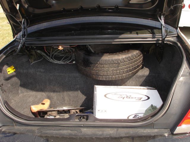 Trunk of a car with a spare tire, a box labeled 'Eagle', and some wiring