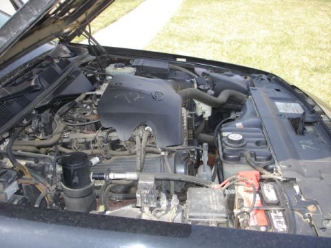 2001 Ford Crown Victoria - The engine bay of a vehicle is shown with various components including hoses, the battery, and an engine cover.