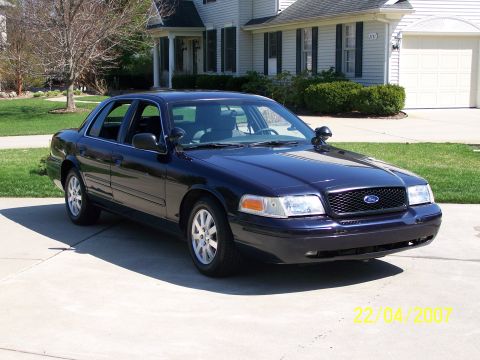 2003 Ford Crown Victoria - A dark blue 2003 Ford Crown Victoria is parked in front of a suburban home.