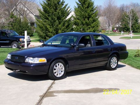 2003 Ford Crown Victoria - A dark purple 2003 Ford Crown Victoria sedan is parked on a concrete driveway with a house and trees in the background.