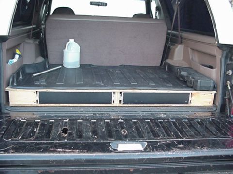 1993 Ford Bronco - View through the open rear tailgate of a Ford Bronco SUV, showing the cargo area with a custom plywood-framed storage drawer platform holdi…