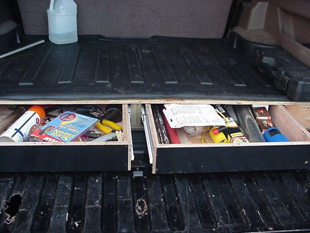 Custom wooden two-drawer storage slide in a vehicle cargo bed, drawers open showing tools