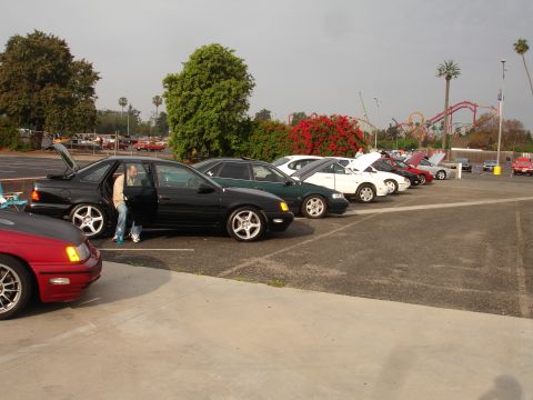 1993 Ford Taurus - A line of cars are parked in a lot, with a person getting out of a black sedan.