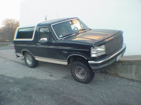 1993 Ford Bronco - Three-quarter front view of a black full-size Ford Bronco with a white removable hardtop and tan lower body stripe, parked on asphalt next…