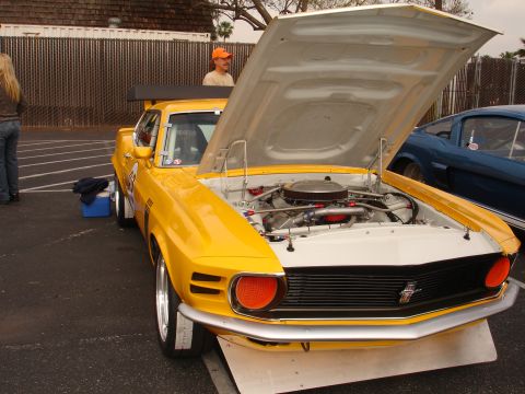 1993 Ford Taurus - A yellow 1969 Ford Mustang Boss 302 race car is parked with its hood open, revealing the engine, next to a blue car.