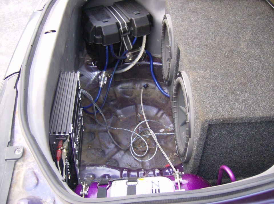 Car trunk interior with two subwoofers, an amplifier, and a purple air tank