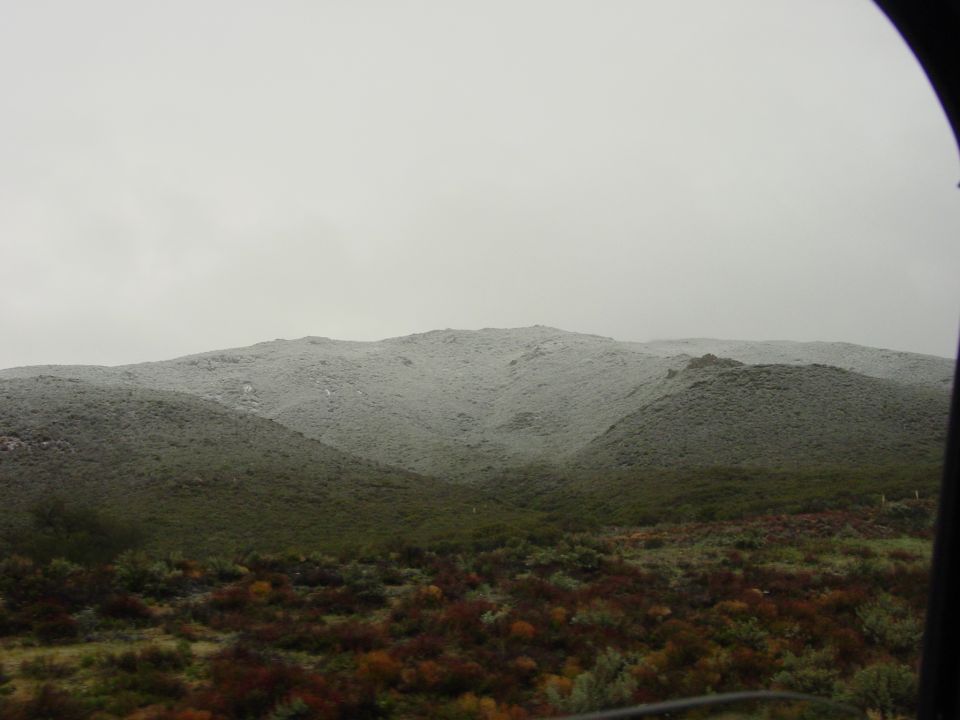 Overcast sky above snow-dusted hills and green foliage