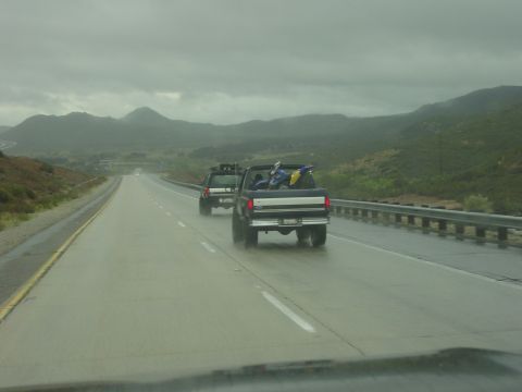 1994 Ford Bronco - Two SUVs travel down a highway on a cloudy day, with one truck bed loaded with dirt bikes.