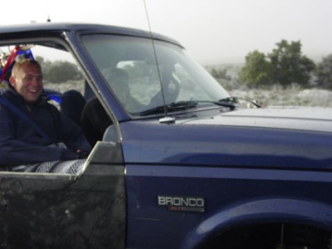 1994 Ford Bronco - A man smiles from the driver's seat of a blue 1994 Ford Bronco on a foggy day.