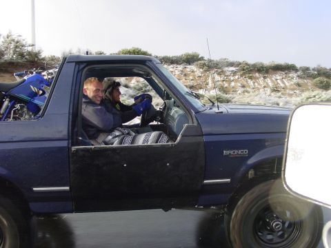 1994 Ford Bronco - A blue Ford Bronco drives down a road with a motorcycle loaded in the rear cargo area.