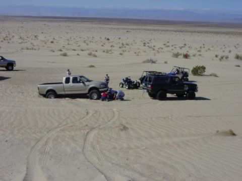 1994 Ford Bronco - Several vehicles are gathered in a desert landscape, including a black Ford Bronco and a silver pickup truck.
