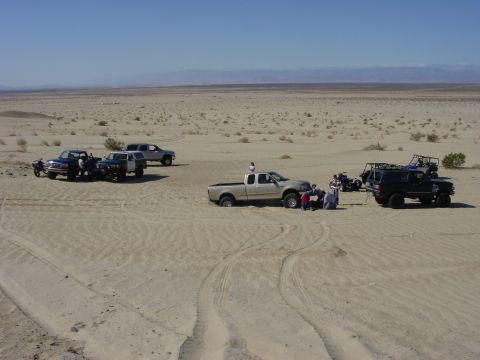 1994 Ford Bronco - A group of trucks, SUVs, and ATVs are parked in a sandy desert area under a clear blue sky.