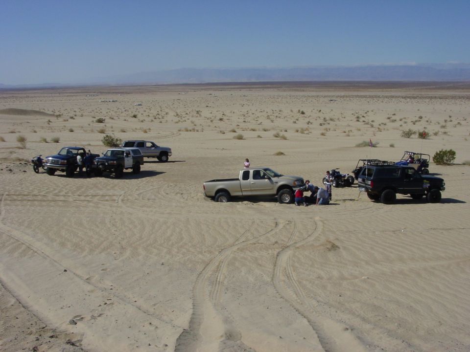 Several off-road vehicles gathered in a desert with people around