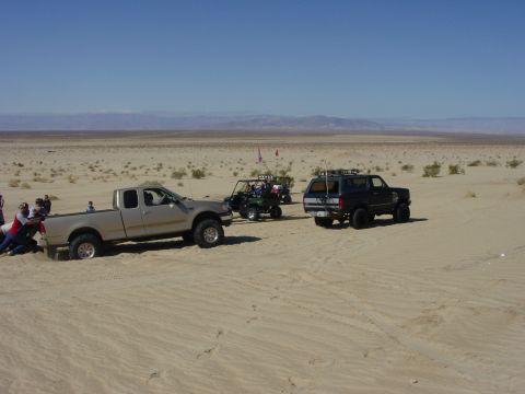 1994 Ford Bronco - Several off-road vehicles are gathered in a sandy desert landscape under a clear blue sky.