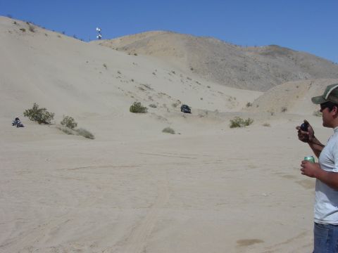 1994 Ford Bronco - A dark Ford Bronco navigates sandy terrain with a person holding a camera in the foreground.