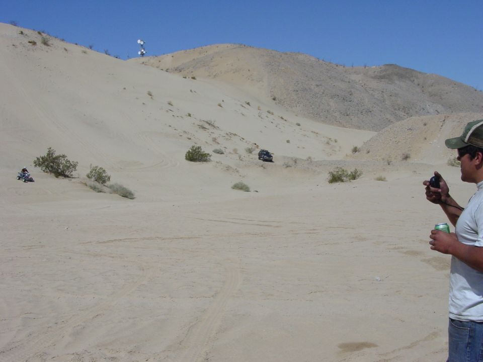 Dark-colored 1992 Ford Bronco driving on sand dunes, side view