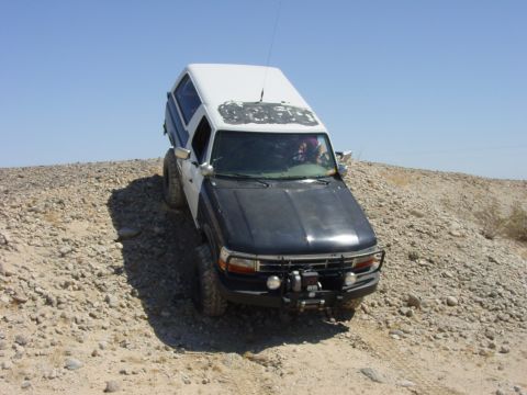 1994 Ford Bronco - This modified Ford Bronco navigates a challenging, rocky terrain under a clear blue sky.