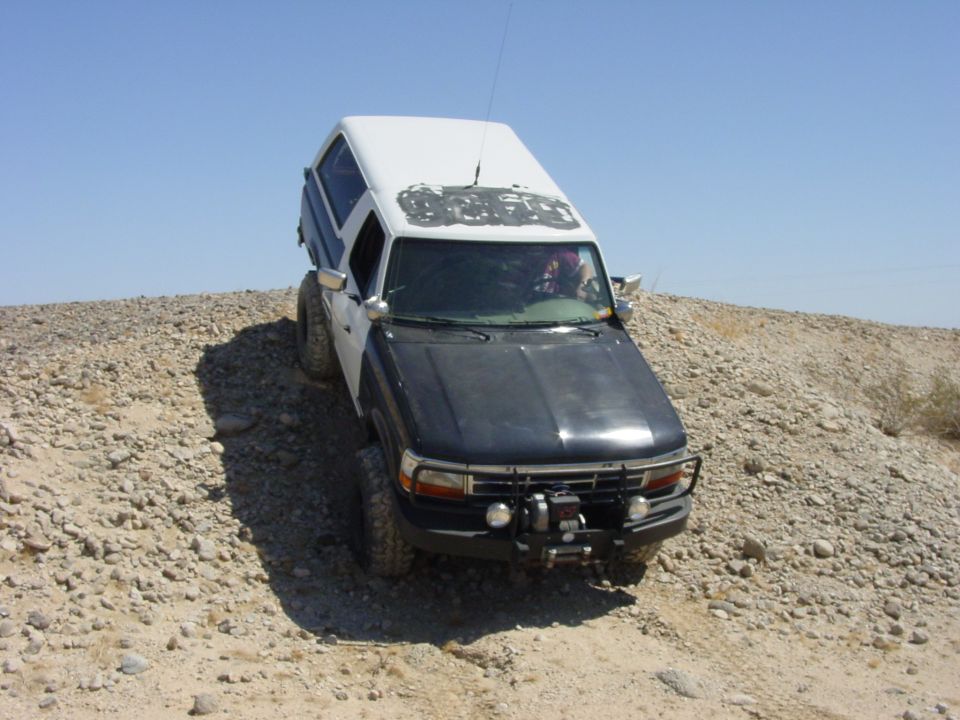 White and black Ford Bronco with a winch on the front bumper, driving on a rocky hill
