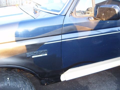1993 Ford Bronco - Close-up of a dark blue 1993 Ford Bronco's fender, showing the "Bronco" emblem and silver accent trim.