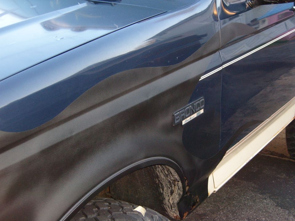 Side view of a 1993 Ford Bronco with a dark blue body and a cream-colored lower trim. The 'BRONCO' badge is visible on the fender
