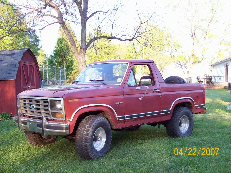 Red Ford Bronco with a spare tire in the bed, parked on grass