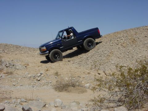 1994 Ford Bronco - 1994 Ford Bronco navigates a challenging off-road trail on a sunny day.