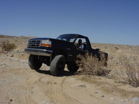 1994 Ford Bronco - A black Ford Bronco navigates a dusty, off-road trail under a clear blue sky.