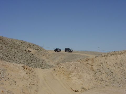 1994 Ford Bronco - Two SUVs traverse a remote dirt road, highlighting the arid, mountainous terrain under a vast expanse of blue sky.