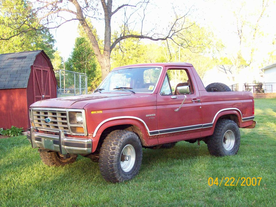 1986 Ford Bronco parked on grass next to a red shed