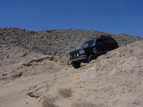 1994 Ford Bronco - A black SUV navigates a steep, sandy incline under a clear blue sky.