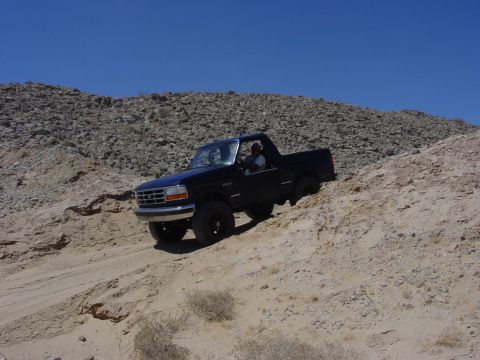 1994 Ford Bronco - A black Ford Bronco navigates a steep, sandy incline under a clear blue sky.