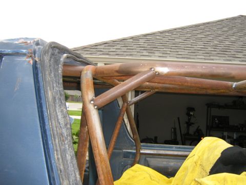 1986 Ford Bronco - The interior of a blue SUV shows a custom, rusty roll cage installed over a yellow tarp.