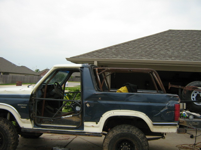 Side view of a blue and white Ford Bronco with a roll cage installed. The doors are off