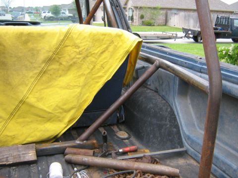 1986 Ford Bronco - The interior of a vehicle shows a roll cage and a yellow tarp covering the seat, with tools scattered on the floor.