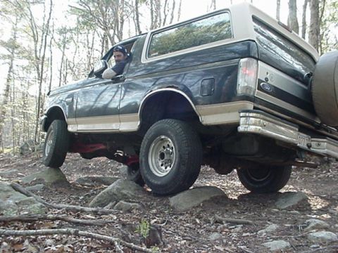 1993 Ford Bronco - A 1993 Ford Bronco navigates a rocky path in a wooded area.