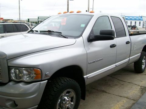 2005 Dodge 3500 - A silver 2005 Dodge Ram 3500 pickup truck is parked on a concrete lot, with another vehicle visible in the background.