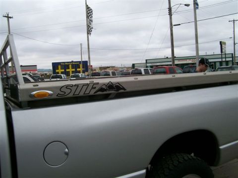 2005 Dodge 3500 - Close-up of a silver pickup truck's bed and rack, the STF logo. Other vehicles are visible in the background.