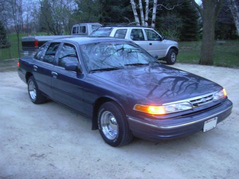 1996 Ford Crown Victoria - A dark blue sedan is parked outside with other vehicles in the background.
