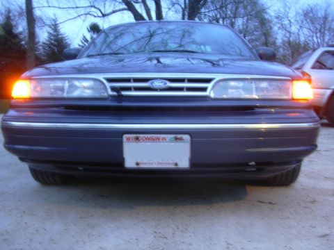 1996 Ford Crown Victoria - Front view of a dark blue Ford Crown Victoria with its left turn signal on. Another vehicle is partially visible to the right.