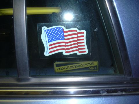 1996 Ford Crown Victoria - A sticker of the American flag is placed on the window of a vehicle, above a 'Police Interceptor' badge.