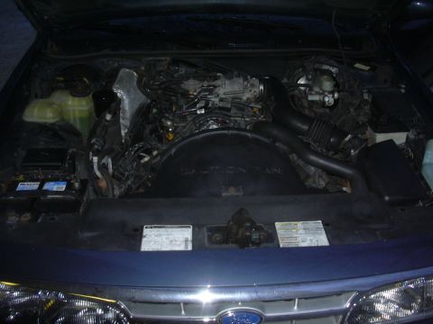 1996 Ford Crown Victoria - The engine bay of a blue vehicle is shown, with various mechanical parts and wiring visible.