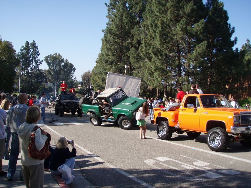 Green off-road vehicle with hood open and orange pickup truck in a parade